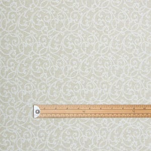 May include: A close-up of fabric featuring a repeating white scroll pattern on a pale green backdrop. A wooden ruler with markings in inches is placed on the fabric, showing measurements.