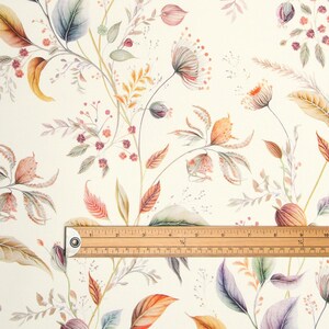 May include: Fabric with a cream background, adorned with watercolour illustrations of leaves, flowers, and berries in orange, purple, and green hues. A wooden ruler is placed across the fabric, measuring up to 25 cm.