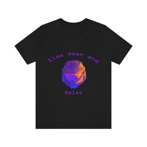Può includere: T-shirt nera con la scritta viola "Slow down and Relax" che incornicia un design geometrico a forma di casco. Il casco presenta sfumature di blu, viola e giallo.