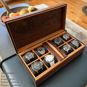 Puede incluir: Una caja de reloj de madera con tapa con bisagras, con un exterior marrón oscuro y un interior de madera más clara. La caja está dividida en compartimentos, cada uno con un reloj de pulsera. La caja contiene ocho relojes.