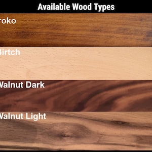 May include: A chart titled Available Wood Types displaying four horizontal wood grain samples. The labels are Iroko, Birtch, Walnut Dark, and Walnut Light. Each section shows the distinct color and texture of the wood, ranging from light beige to dark brown tones.