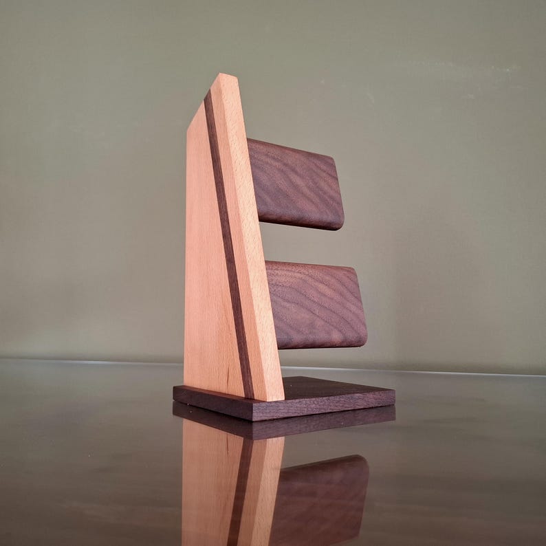 Op de afbeelding: Een houten horlogestandaard met een licht houten frame en donkere houten accenten. De standaard heeft twee donkere houten platforms voor het vasthouden van horloges. Het ontwerp omvat een donkere houten basis en een verticale lichte houten steun met een donkere houten streep.