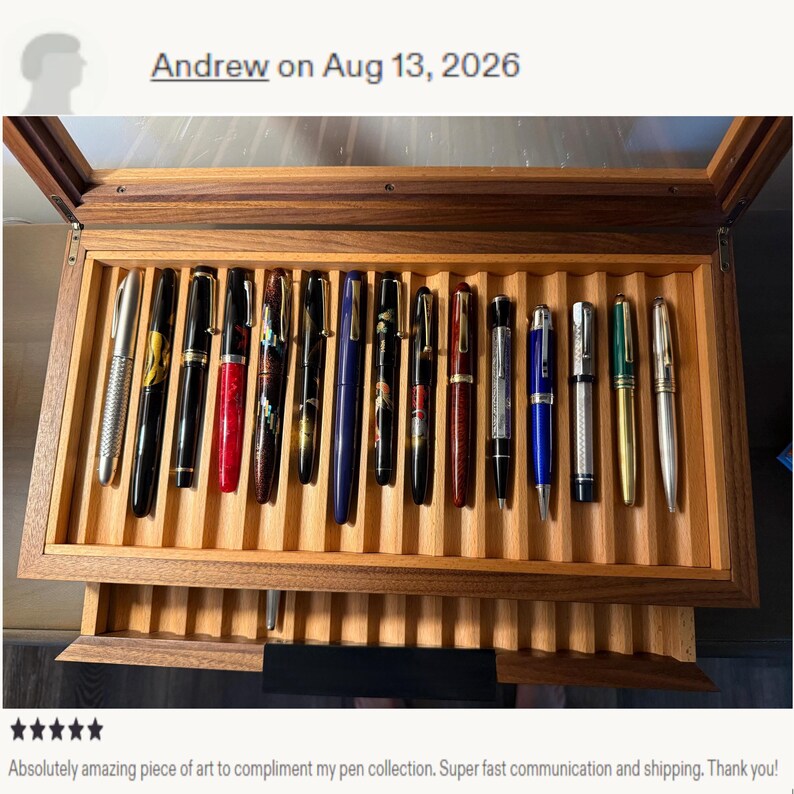 May include: A wooden display case with a glass lid containing fourteen fountain pens arranged in individual slots. The pens feature various colors and finishes, including silver, black, red, blue, and green, with gold or silver-toned clips.