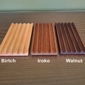 Pode incluir: Tr&ecirc;s bandejas de madeira com uma borda ondulada e uma superf&iacute;cie estriada. As bandejas s&atilde;o etiquetadas como "Birtch", "Iroko" e "Walnut".