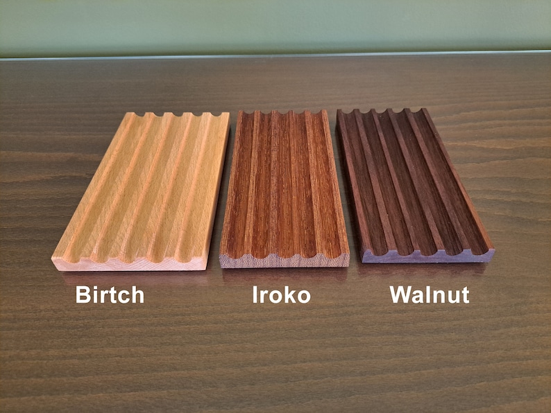 Pode incluir: Tr&ecirc;s bandejas de madeira com uma borda ondulada e uma superf&iacute;cie estriada. As bandejas s&atilde;o etiquetadas como "Birtch", "Iroko" e "Walnut".