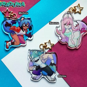 Può includere: Tre portachiavi con personaggi colorati e ciondoli a forma di stella dorata. I personaggi sono un lupo blu e bianco, una volpe rosa e bianca e un procione blu e rosso. I portachiavi sono su uno sfondo rosa e blu.