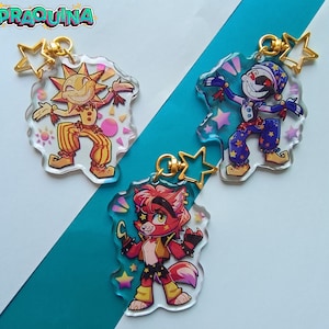 Puede incluir: Tres llaveros de personajes coloridos con cadenas doradas y dijes de estrellas. Los personajes son un bufón rojo y amarillo, un bufón azul y morado y un zorro rojo y naranja.