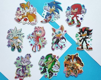 Może przedstawiać: Zestaw dziesięciu holograficznych naklejek z postaciami z serii gier wideo Sonic the Hedgehog. Naklejki są wydrukowane na przezroczystym tle i przedstawiają różne postacie, w tym Sonica, Tailsa, Knucklesa, Amy, Shadowa, Rouge i wiele innych.
