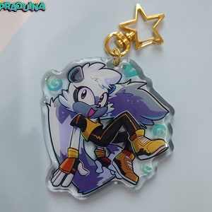 Op de afbeelding: Een transparante sleutelhanger met een gouden sterbedel waarop een paars-wit cartoonfiguur met een geel-zwarte outfit te zien is. Het figuur heeft een witte staart en draagt sneakers.
