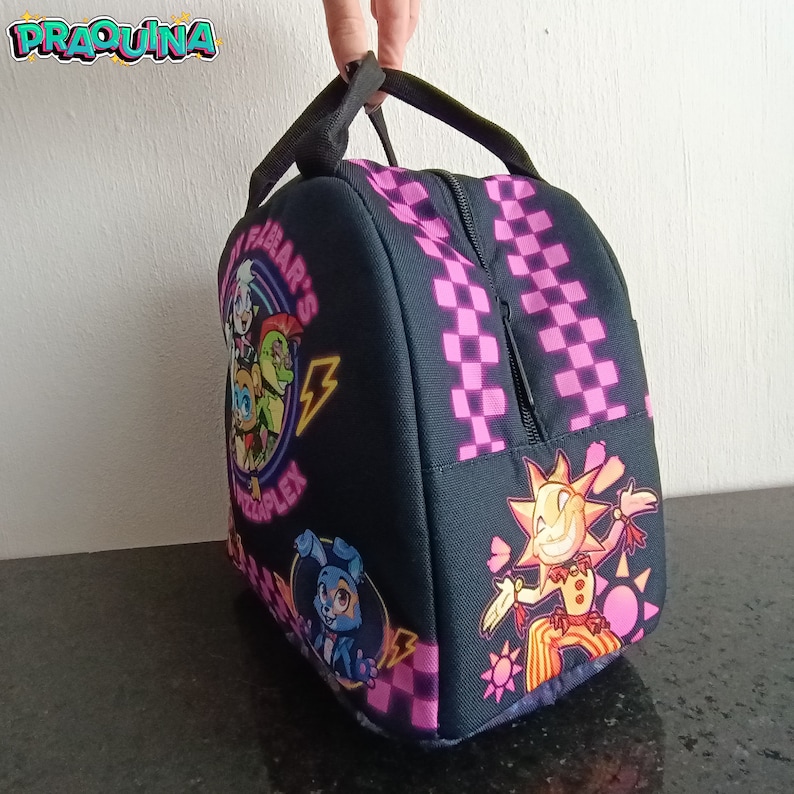 Peut inclure: Sac &agrave; d&eacute;jeuner &agrave; carreaux noirs et roses avec un imprim&eacute; graphique de personnages de dessins anim&eacute;s et le texte "Fazbear's Pizzaplex".