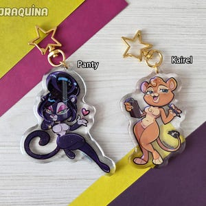 May include: Two acrylic keychains featuring cartoon characters. One keychain depicts a purple panther-like character named "Panty" with a heart. The other keychain shows a lioness character named "Kairel" holding a clipboard and pen. Both have gold star-shaped clasps.