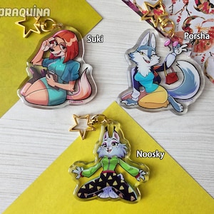 May include: Three clear acrylic keychains with cartoon characters. "Suki" is a fox with red hair and glasses. "Porsha" is a wolf with a purse. "Noosky" is a wolf in a green jacket and patterned trousers. Each keychain has a gold star charm.