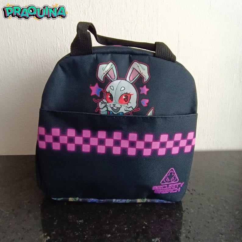 Peut inclure: Sac &agrave; d&eacute;jeuner noir avec un motif &agrave; carreaux rose et blanc. Il repr&eacute;sente un lapin de dessin anim&eacute; avec des yeux rouges et un n&oelig;ud papillon rose. Le sac a une poign&eacute;e noire et le texte "Security Breach" en bas.