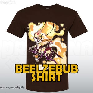 May include: A brown t-shirt with a cartoon illustration of a character with yellow hair and a dessert. The text "BEELZEBUB SHIRT" is displayed in yellow block letters. The phrase "*colors may vary slightly" is at the bottom.