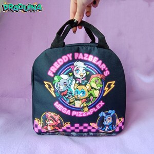 Peut inclure: Sac &agrave; d&eacute;jeuner noir avec un graphisme color&eacute; de cinq personnages de dessin anim&eacute; du jeu vid&eacute;o "Freddy Fazbear's Mega Pizzaplex". Les personnages sont dispos&eacute;s en cercle avec le texte "Freddy Fazbear's Mega Pizzaplex" en lettres n&eacute;on roses.