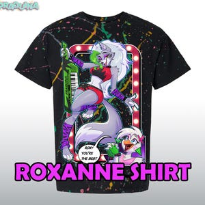 Könnte beinhalten: Schwarzes T-Shirt mit einem farbenfrohen Spritzmuster. Das Shirt zeigt eine Grafik eines Cartoon-Wolfs, der ein Keyboard spielt, mit dem Text "ROXANNE SHIRT" in großen rosa Buchstaben. Ein kleinerer Cartoon-Hühner ist ebenfalls vorhanden.