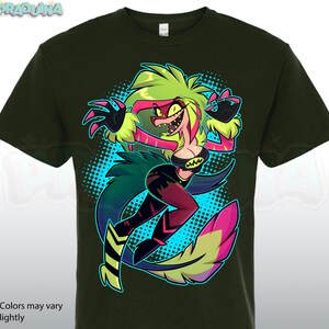 May include: Dark green t-shirt featuring a colorful cartoon character with green, pink, and yellow hair and a black outfit. The character is set against a blue dotted background. The text "*Colors may vary slightly" is at the bottom.