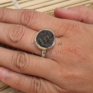 May include: A silver ring with a round black stone set in a silver bezel. The ring is on a person's finger.
