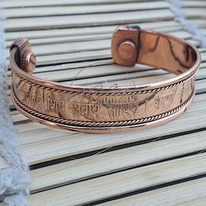 May include: A copper bracelet with a magnetic clasp and an inscription in Sanskrit. The inscription reads "Om Gam Ganapataye Namaha".