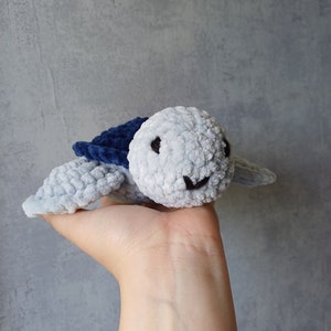 Peut inclure: Une tortue en peluche crochetée de couleur bleu clair et bleu foncé avec des yeux noirs et une bouche souriante.