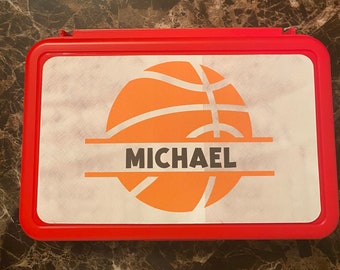 May include: Red plastic lunchbox with a white sticker featuring an orange basketball with black lines and the name "MICHAEL" in black text.