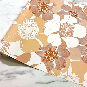 May include: A vintage wallpaper roll featuring a floral design. The flowers are white with orange centres and are set against a peach background.