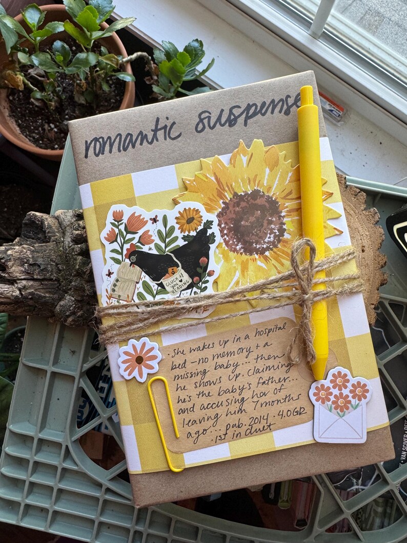May include: A book wrapped with twine, featuring the words "romantic suspense". It's decorated with a sunflower, stickers, and a yellow pen. The book has a yellow and white checkered pattern. Text on the book reads: "She wakes up in a hospital bed..."