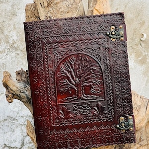 May include: A brown leather journal with a tree of life design embossed on the front cover. The journal has two metal clasps and a decorative border.