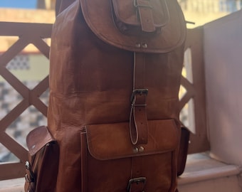 May include: A brown leather backpack with multiple pockets and buckles. The backpack has a flap with a buckle closure and a smaller pocket on the front.