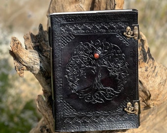 May include: Black leather journal with a tree of life design and a red stone accent. The journal has two brass clasps.