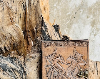 May include: A brown leather journal with a tooled design of two dragons intertwined. The journal has a brass clasp and a decorative border.