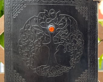 May include: Black leather journal with an embossed tree of life design and a red gemstone accent. The journal has two metal clasps.