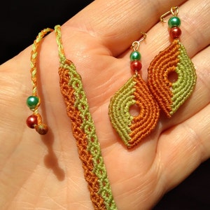 Può includere: Un set di gioielli fatti a mano con un braccialetto verde e arancione e orecchini abbinati. Gli orecchini sono realizzati con un design in macramé verde e arancione e hanno una piccola perla verde e una perla rossa su ogni orecchino.