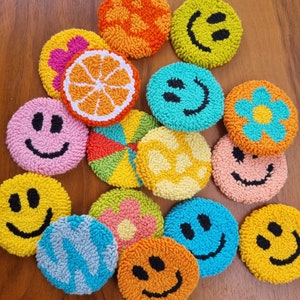 May include: A collection of 14 colorful, round, hand-stitched felt ornaments. The ornaments feature various designs, including smiley faces, flowers, and a slice of orange.
