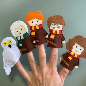 Op de afbeelding: Vijf vingerpoppen van vilt van Harry Potter-personages. De personages zijn Harry Potter, Ron Wemel, Hermelien Griffel, Albus Perkamentus en Hedwig de uil. De poppen zijn bruin, rood en wit.