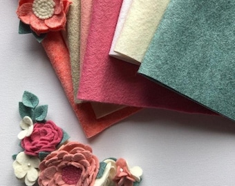Op de afbeelding: Assortiment van viltstofplaten in verschillende tinten roze, perzik, beige, crème en groen. De viltstofplaten zijn in een waaier vorm gerangschikt, met de groene plaat onderaan. Er zijn ook viltbloemversieringen.