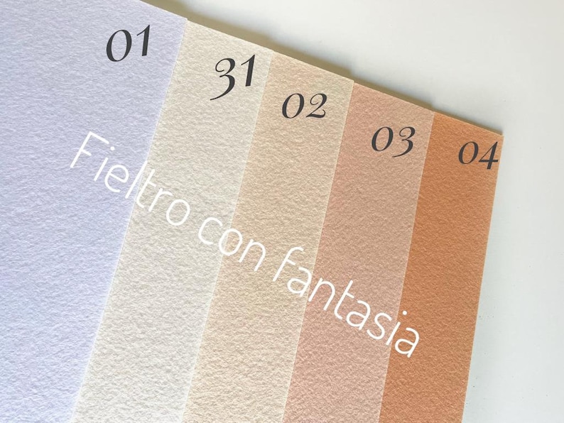 May include: Four samples of felt fabric in different colors: light purple, white, light beige, and light brown. The samples are labeled with numbers 01, 31, 02, 03, and 04. The text "Feltro con fantasia" is written on the samples.