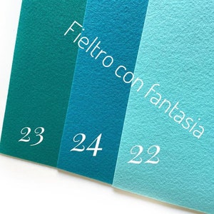 May include: Three felt fabric swatches in shades of teal and turquoise. The swatches are labeled with the numbers 23, 24, and 22. The text "Feltro con fantasia" is written diagonally across the swatches.