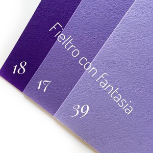 May include: Three swatches of felt fabric in shades of purple. The swatches are labeled with the numbers 18, 17, and 39. The text "Feltro con fantasia" is written on the swatches.