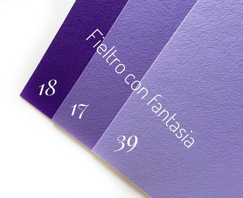 May include: Three swatches of felt fabric in shades of purple. The swatches are labeled with the numbers 18, 17, and 39. The text "Feltro con fantasia" is written on the swatches.