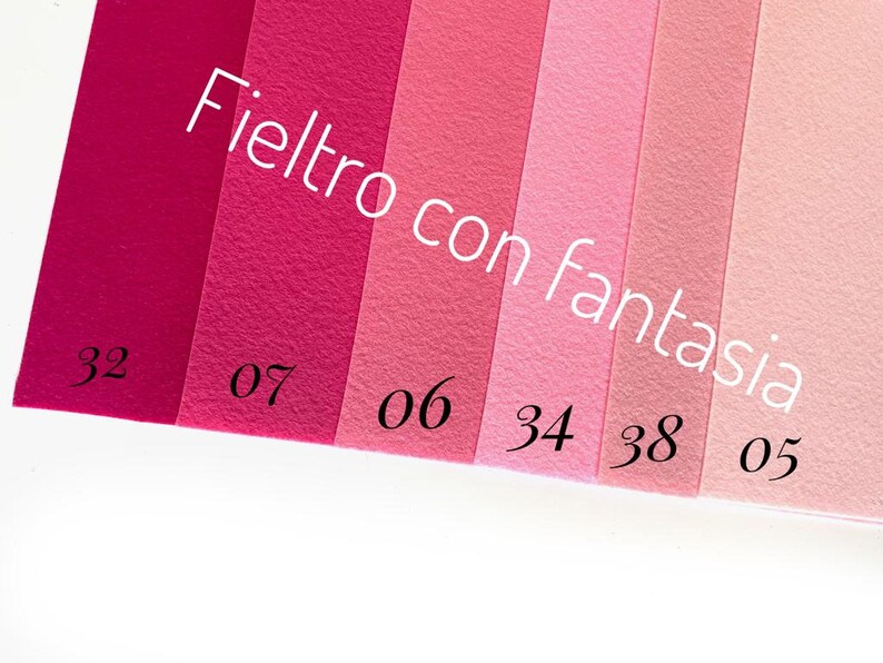 May include: A color chart of felt fabric swatches in various shades of pink, labeled with numbers. The text "Feltro con fantasia" is written in black across the top of the swatches.