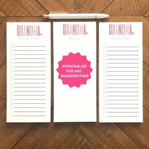 May include: Three white notepads with the word "GRANDMA" in pink and gray, and a pen. One notepad says "Grocery List", another says "Notes" with a pink starburst that says "PERSONALIZE FOR ANY GRANDMOTHER", and the third says "To Do List".