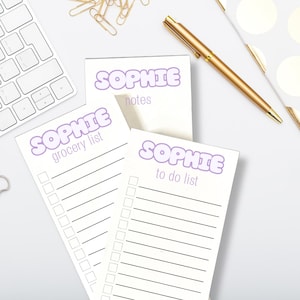 May include: Three white notepad sets with purple text that says "Sophie" and a different list title on each. The list titles are "notes", "grocery list", and "to do list".