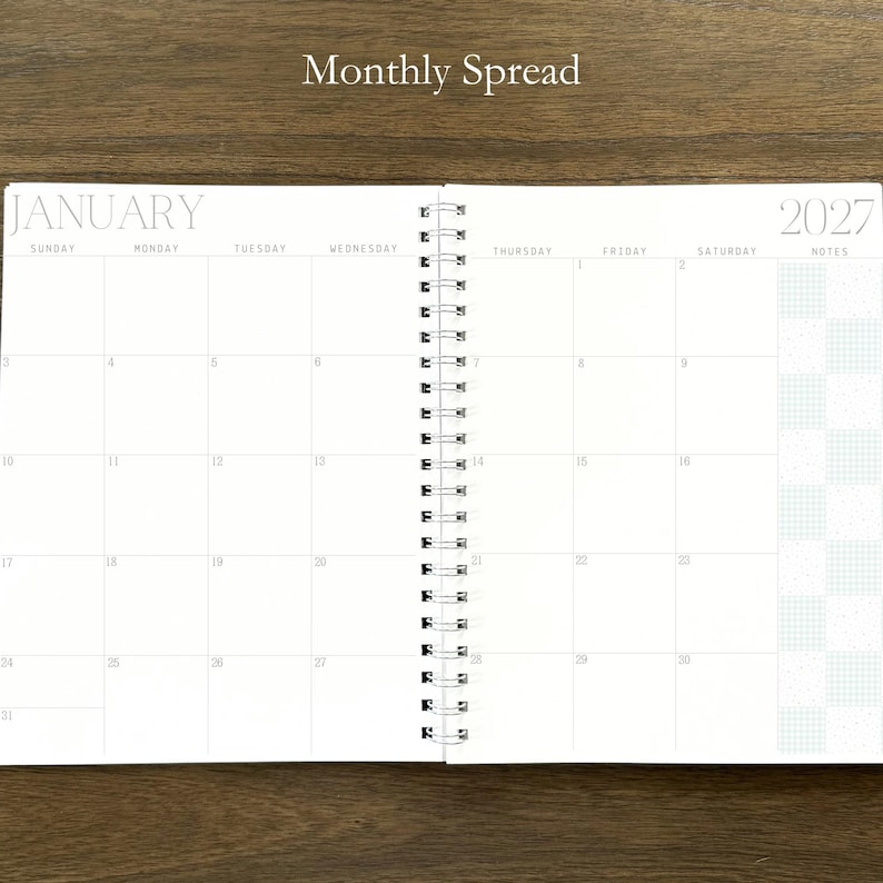 Puede incluir: Una agenda de espiral abierta en una vista mensual para enero de 2027. Las p&aacute;ginas blancas presentan una cuadr&iacute;cula con los d&iacute;as de la semana, fechas numeradas y una columna de notas con un patr&oacute;n de cuadros. El texto Monthly Spread es visible.