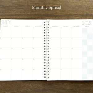 Puede incluir: Una agenda de espiral abierta en una vista mensual para julio de 2026. Las p&aacute;ginas blancas presentan un dise&ntilde;o de cuadr&iacute;cula con los d&iacute;as de la semana de domingo a s&aacute;bado, una columna de notas a la derecha y el texto Monthly Spread arriba.