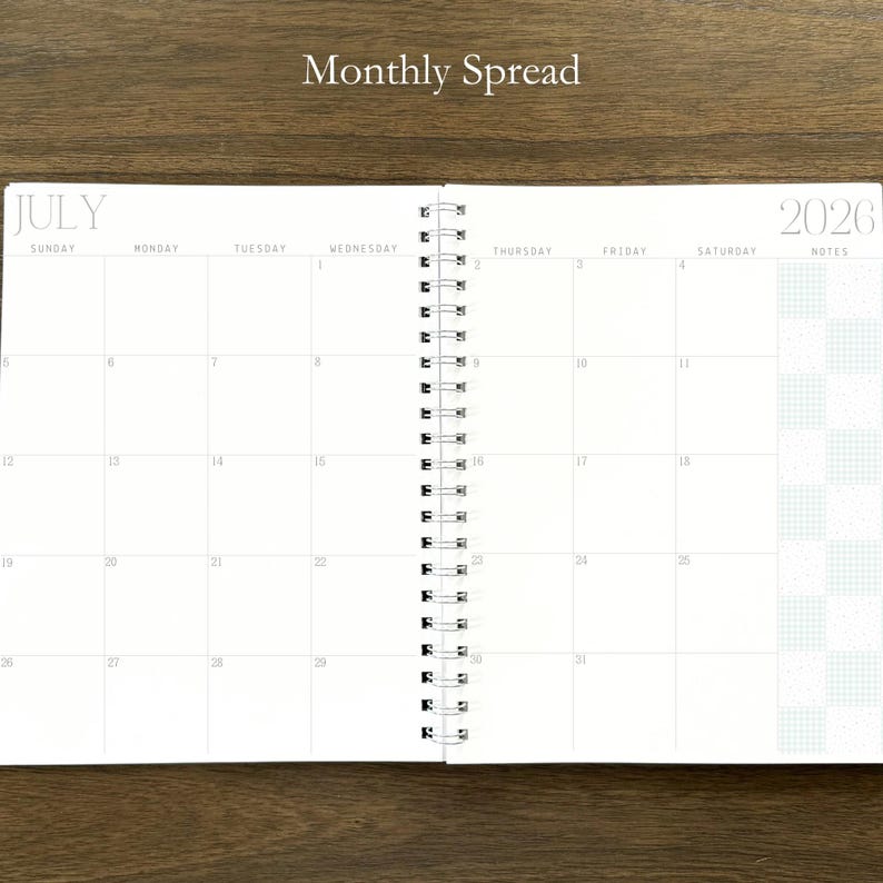 Puede incluir: Una agenda de espiral abierta en una vista mensual para julio de 2026. Las p&aacute;ginas blancas presentan un dise&ntilde;o de cuadr&iacute;cula con los d&iacute;as de la semana de domingo a s&aacute;bado, una columna de notas a la derecha y el texto Monthly Spread arriba.