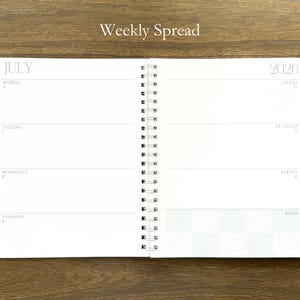 Puede incluir: Una agenda de espiral abierta en una vista semanal para julio de 2026. La p&aacute;gina izquierda enumera del lunes 6 al jueves 9, mientras que la derecha enumera del viernes 10 al domingo 12 con una secci&oacute;n de notas con un patr&oacute;n de cuadros azul claro.