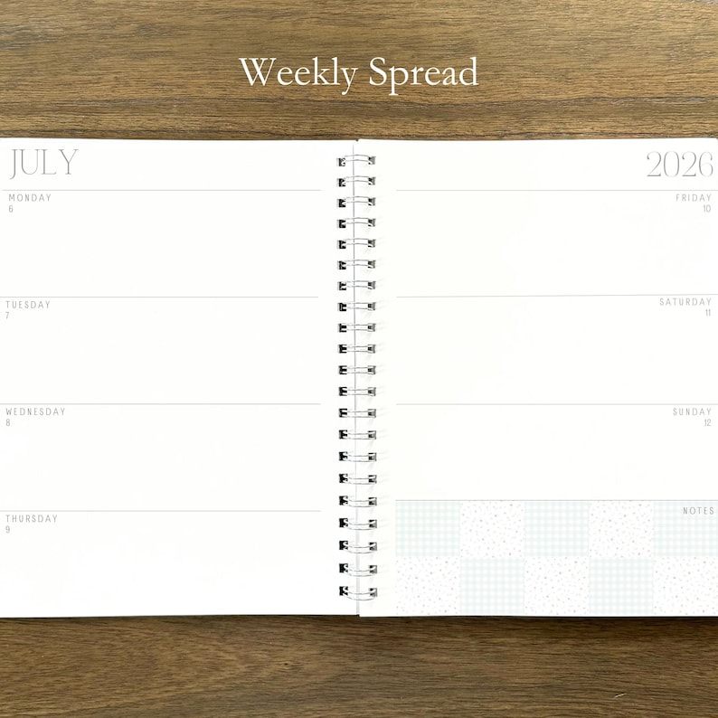 Puede incluir: Una agenda de espiral abierta en una vista semanal para julio de 2026. La p&aacute;gina izquierda enumera del lunes 6 al jueves 9, mientras que la derecha enumera del viernes 10 al domingo 12 con una secci&oacute;n de notas con un patr&oacute;n de cuadros azul claro.