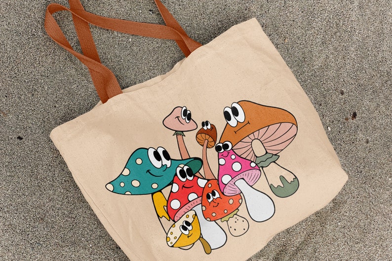 May include: A beige canvas tote bag with a colorful cartoon design of mushrooms with googly eyes. The mushrooms are various colors, including red, orange, green, and yellow.