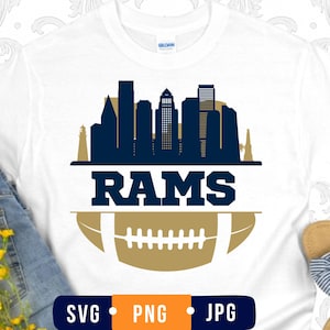 May include: A white t-shirt featuring a dark blue city skyline silhouette above the word RAMS in bold dark blue capital letters, positioned over a gold football graphic with white laces. The bottom includes a dark blue label with SVG, PNG, JPG.
